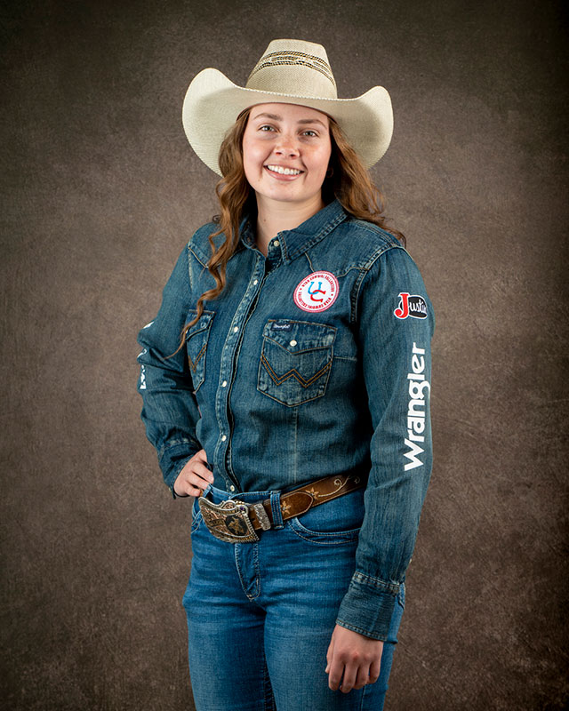 Annie Roper smiling at the camera, posing wearing a denim shirt and cowgirl hat.